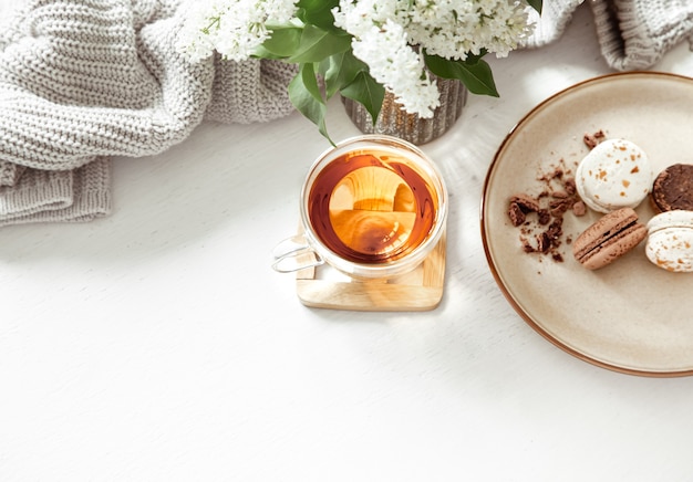 Cozy spring composition with a cup of tea and french macaroons on a white table.