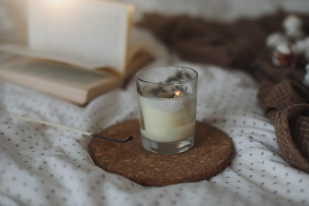 Cozy still life interior details with a book candle and a cotton twig in warm soft bed Sweet home