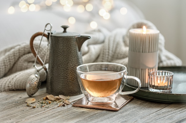 사진 보케가 있는 흐릿한 배경에 차 한 잔, 찻주전자, 촛불이 있는 아늑한 정물.