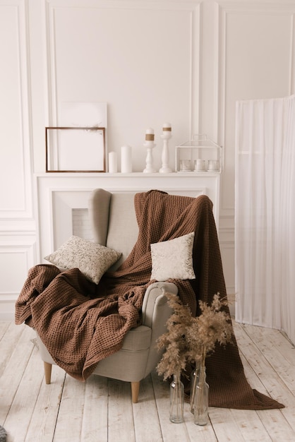 Cozy and stylish interior with an armchair a blanket and books on a light background