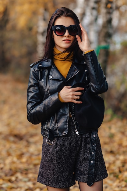 Cozy stylish young girl walk at autumn colorful park in sunglasses