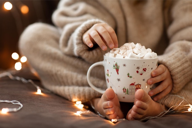 Photo cozy vibes children bare feet and hands hold christmas cup hot cocoa marshmallow in beige sweater