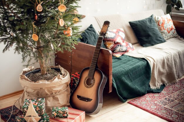 Cozy vintage New Year's interior with a real live Christmas tree loft family celebration at home dried oranges instead of toys guitar retro sofa with decorative pillows