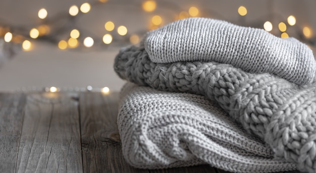 Cozy winter background with a stack of knitted sweaters and lights copy space