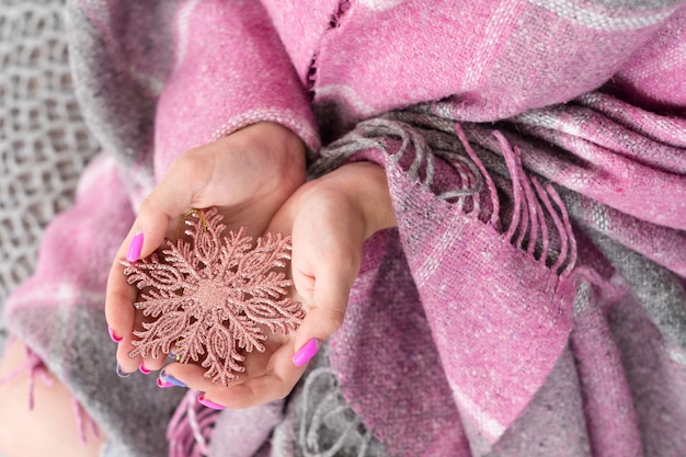 Cozy winter festive time. woman holding a rose gold shiny snowflake in hands covered in warm blanket