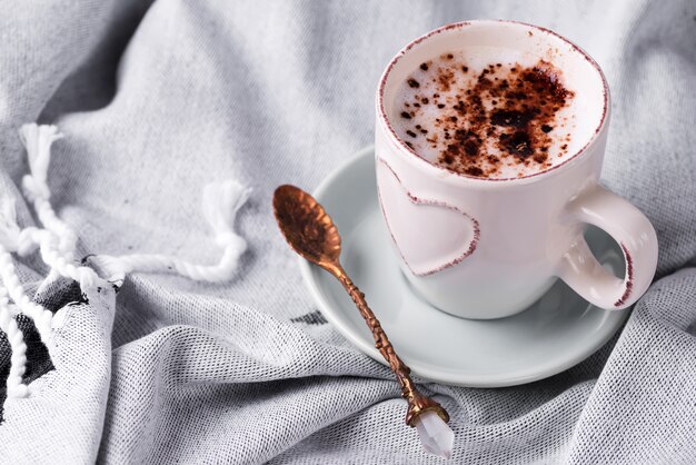 ベッドのある静物シーンで居心地の良い冬の朝の朝食。ウールチェック柄のホットコーヒーまたはココアの蒸しカップ。クリスマス。