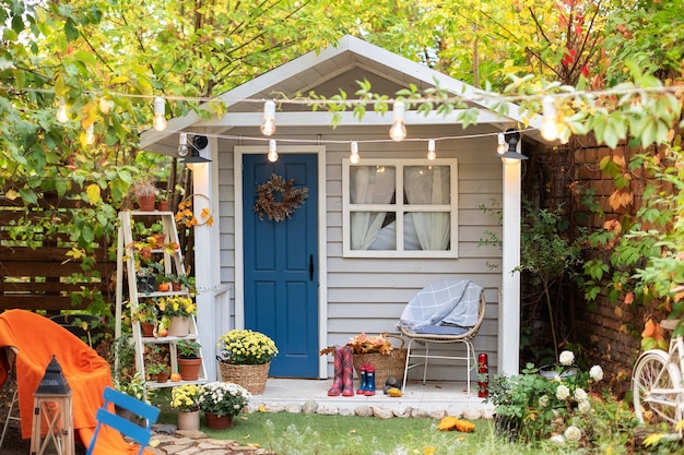 Cozy wooden house porch with chair, potted flowers. Decor of autumn yard