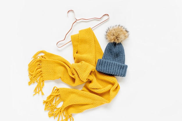 Уютный желтый шарф и синяя шляпа с вешалками на белом фоне. стильный женский осенний или зимний наряд. коллаж модной одежды. плоская планировка, вид сверху.