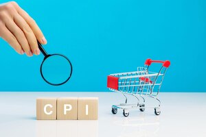 Photo cpi consumer price index symbolletter block in word cpi abbreviation of consumer price index with a magnifying glass in woman's hand near empty shopping cart on blue background