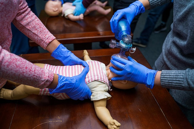 Cpr practitioner examining airway passages on infant dummy.\
model dummy lays on table and two doctors practice first aid.