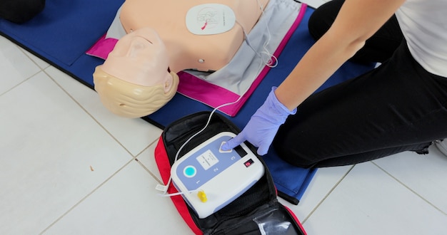 CPR training medical procedure workshop. Demonstrating chest compressions and use of AED automatic defibrillator on CPR doll.