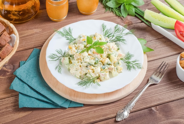 Салат из крабового мяса с огурцами и яйцами, заправленный майонезом, в белой тарелке на темном деревянном фоне