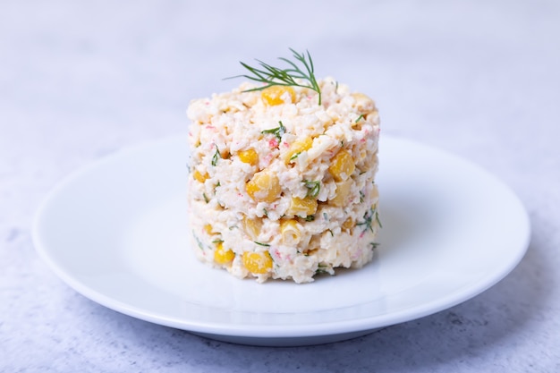 Crab salad with corn and eggs on a white plate. Traditional Russian salad. Close-up.