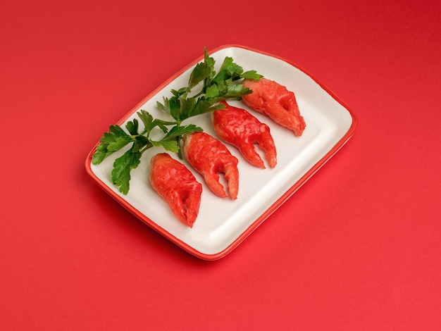 Crab tentacles with parsley leaves in a plate on a bright red background