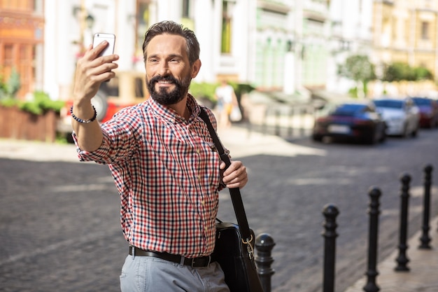 笑顔を割る。通りに立っている間selfiesを作るうれしそうな笑顔の男