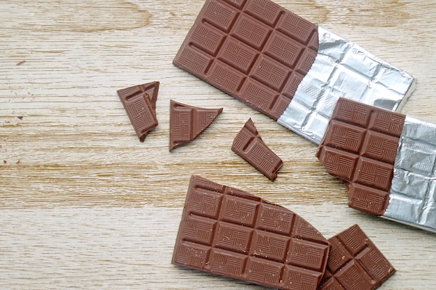 Cracked chocolate bars scattered on wooden background