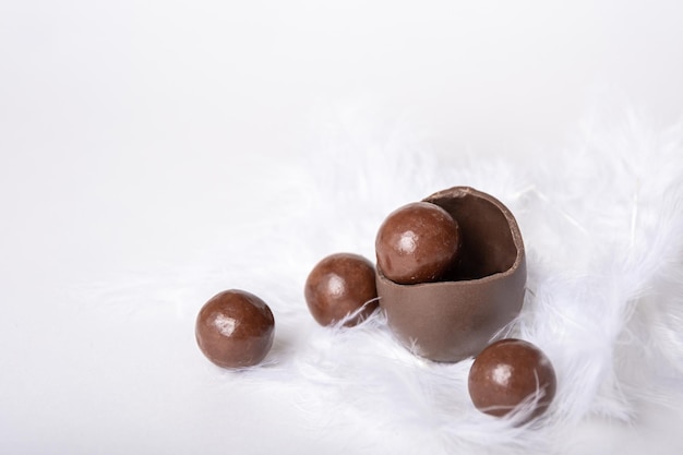 Foto uovo di pasqua al cioccolato incrinato con piccole caramelle rotonde al cioccolato in nido di piume bianche dolcetto al cioccolato per bambini