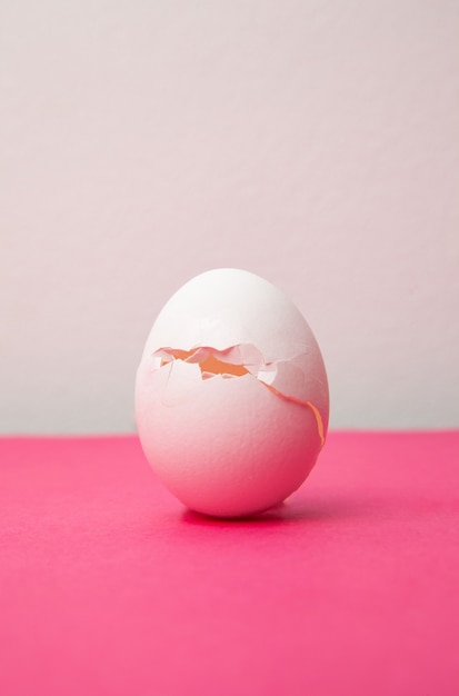 Cracked fresh white egg on pink table