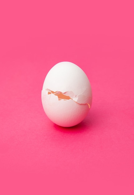 Cracked fresh white egg on pink table