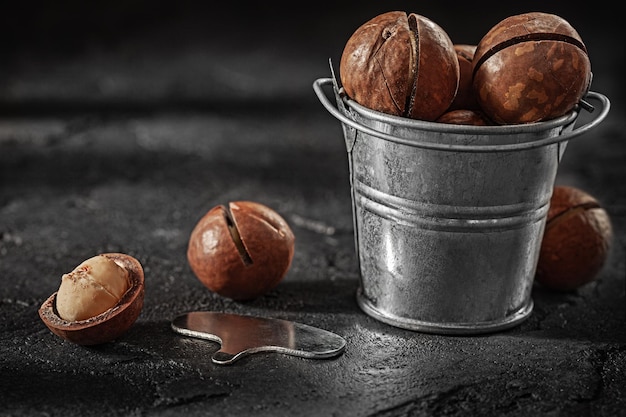 Cracked Macadamia Nuts In Little Bucket On Slate Background