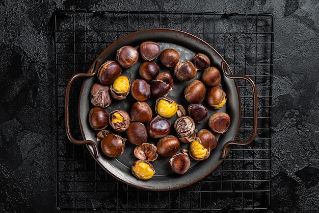 Cracked roast chestnuts served in a tray Black background Top view