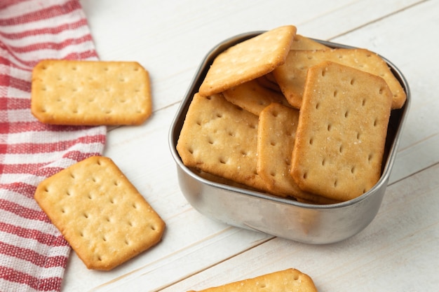 Cracker cookies in een roestvrijstalen kom met tafelkleed op witte houten tafel achtergrond.