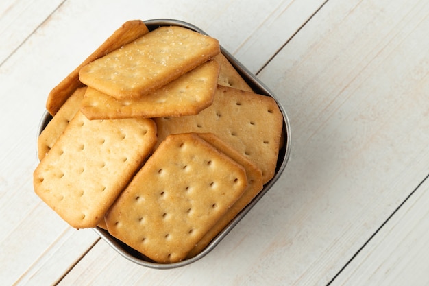 Cracker cookies in a stainless steel bowl on white wooden table background.