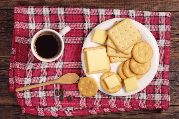 Cracker cookies with cheese and coffee cup on red tablecloth, top view