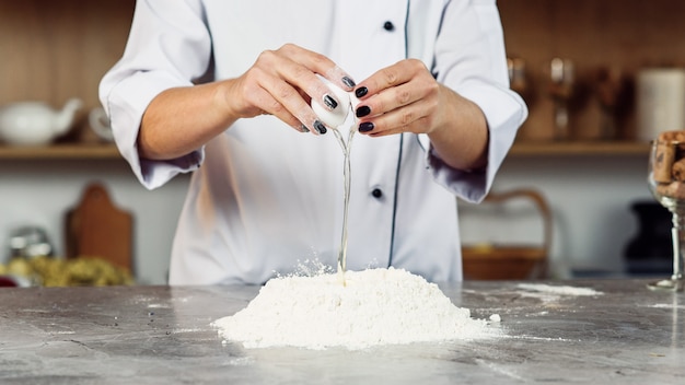 Cracking an egg to a flour. Close-up of woman's hands cracking egg for pastry.