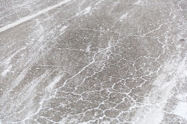 Cracks on the asphalt filled with snow. Low drifting snow on a Winter road texture background