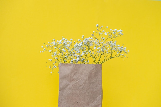 A craft bag with white gypsophila flowers stands on a bright yellow background View from above