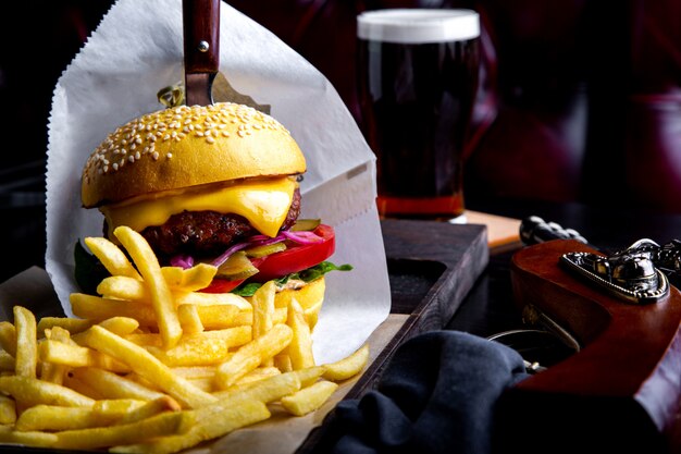 Craft beef burger and french fries on table in restaurant with glass of beer on dark . Modern fast food lunch frame