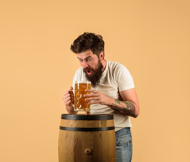 レストランでのクラフトビールは、ビールの木製の樽とビール醸造所のオクトーバーフェストのマグカップで男を驚かせました