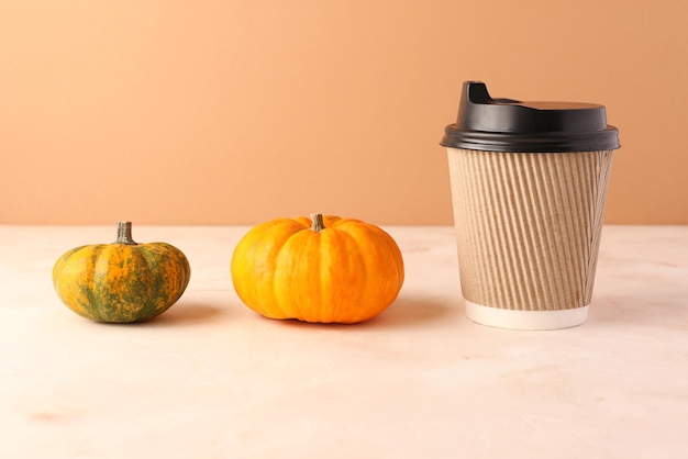 Craft brown paper coffee cup and little decorative pumpkins near it