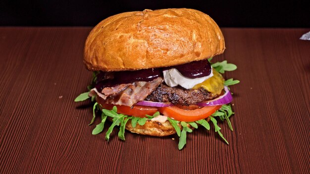 Craft burger is cooking on black background consist sauce\
arugula tomato onion bacon currant sauce ricotta cheese air bun and\
marble meat