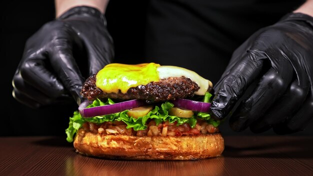 Craft burger is cooking on black background Consist sauce salsa lettuce red onion pickle cheese chilli green pepper bun marbled meat beef