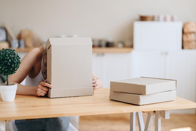 Craft cardboard boxes lie on a natural wooden table in a light interior girl is hiding behind box