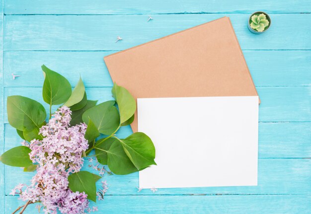 Photo craft envelop, white paper, brunch of lilac, green candle on vintage turquoise wooden background