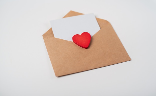 Craft envelope with a blank sheet of paper inside and red paper heart on the light