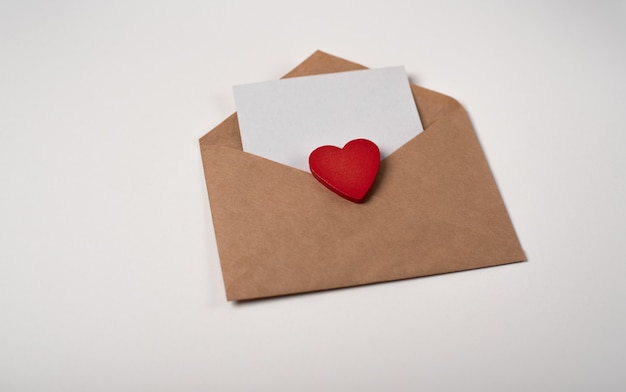 Craft envelope with a blank sheet of paper and a red wooden\
heart. romantic love letter for valentine\'s day concept.