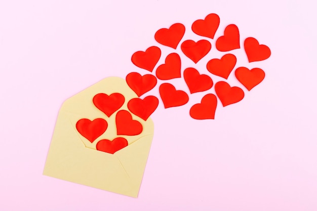 Фото Ремесленный конверт с красными сердечками на пастельно-розовом фоне. плоская планировка, вид сверху. концепция дня святого валентина. концепция дня матери.