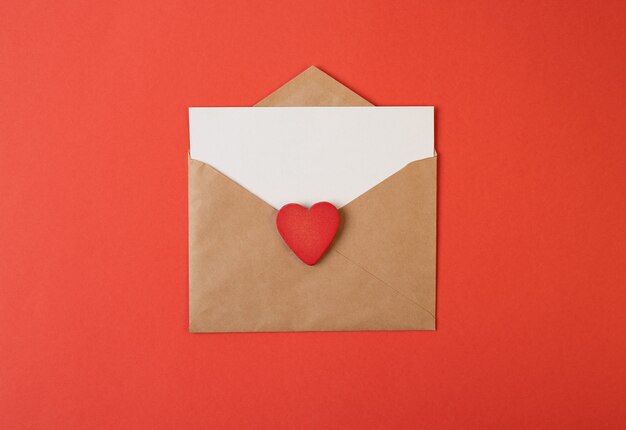 Craft envelope with red Valentine heart and blank white sheet inside on red background.