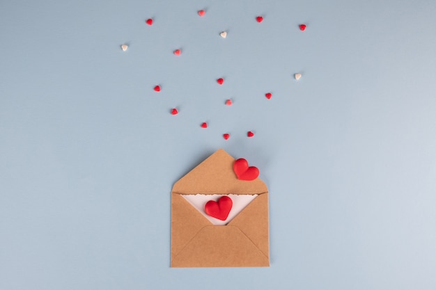 Craft envelope with white blank card and hearts on blue table