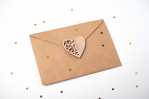 Craft envelope with the wooden heart on it and little golden stars on white. Romantic love letter for Valentine's day concept.
