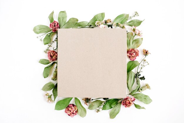 Craft gift box and floral composition with red roses and green leaves on white surface