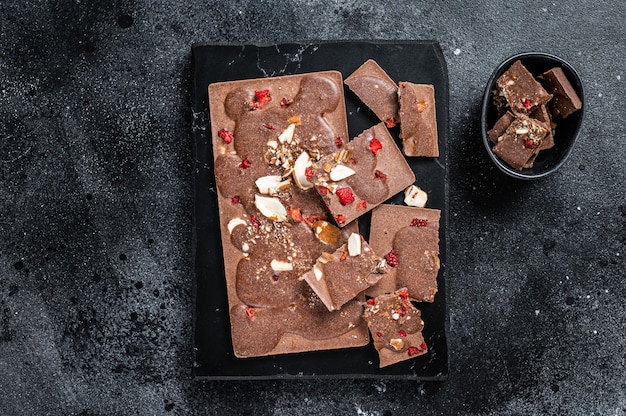 Craft homemade chocolate bars chopped on marble board. Black background. Top view.