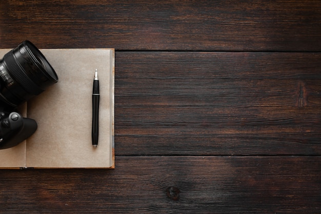 Блокнот, ручка и фотоаппарат на темном деревянном столе