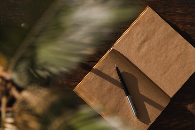 Photo craft notepad with pen on wooden background under palm leaves