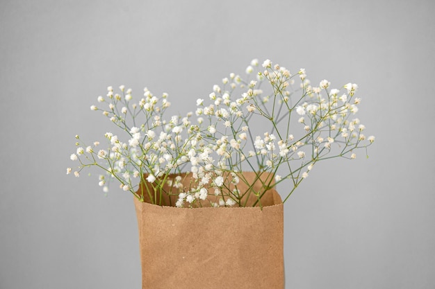 Craft packaging with small white gypsophila flowers on a gray background View from above