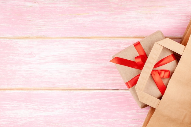 Бумажный пакет и подарочная коробка с красным бантом и сердечками на розовом фоне